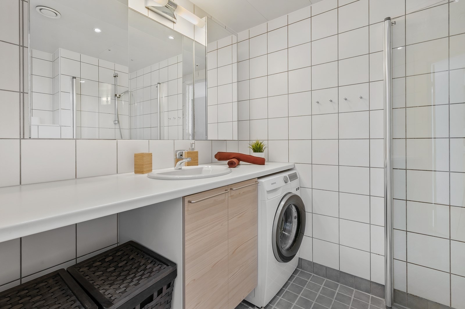 Flislagt og tidløst baderom med opplegg for vaskemaskin, varmekabler i gulvet og dusjhjørnet med svingbare dusjdører. Galleribilde