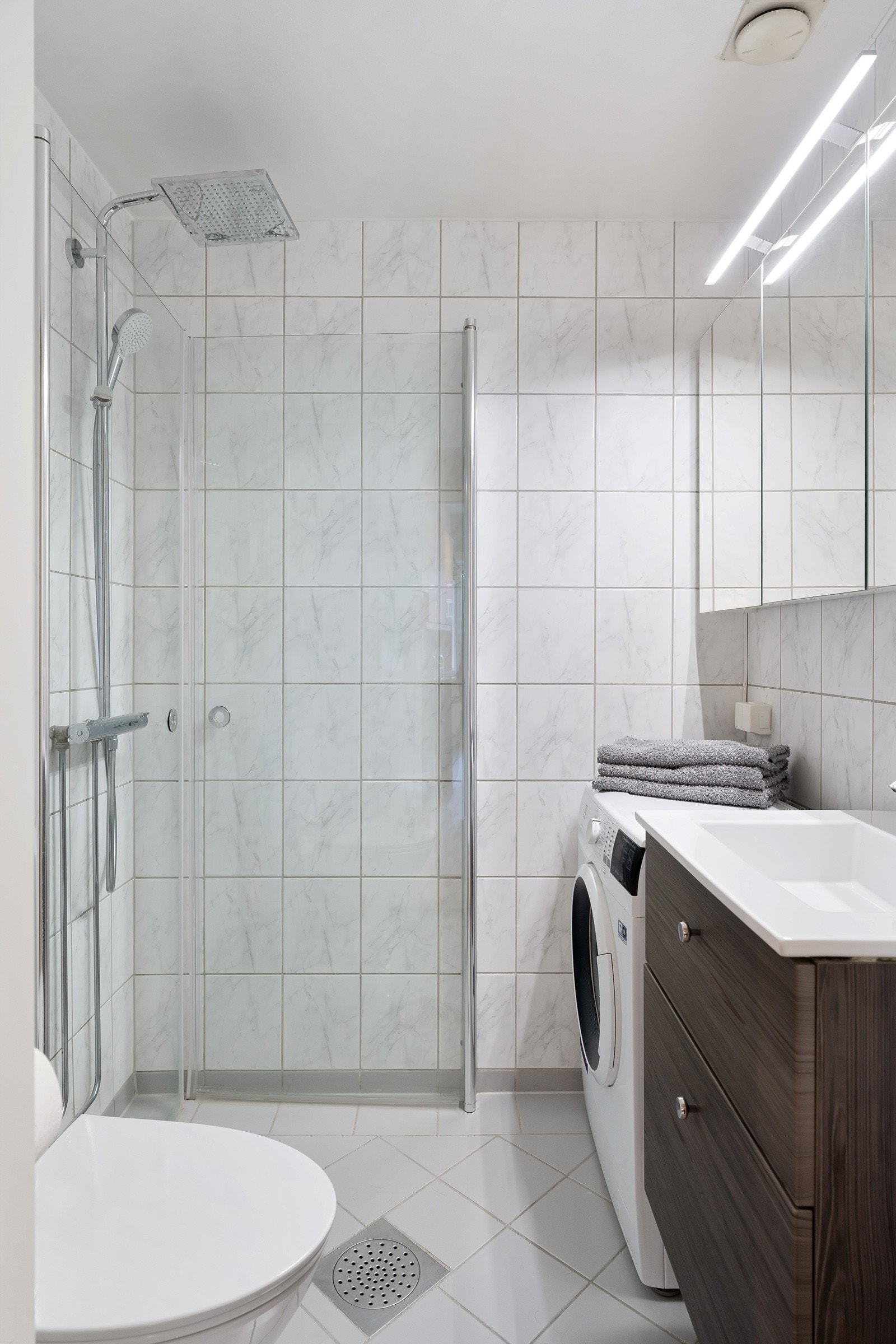 Badet ble renovert i regi av borettslaget i 2001, og er oppgradert med ny innredning i 2021, som inkluderer et toalett, servant på brun skuffeseksjon, nytt blandebatteri og et dusjhjørne med innfellbare glassdører, regnfallsdusj og hånddusj. Galleribilde