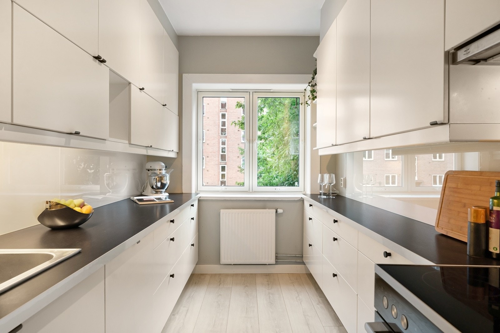 Innredningen fra 2014 er montert parallelt langs to sider og har god arbeidsflyt langs benkeplater i mørk laminat med nedfelt vaskekum i stål. Det er godt med oppbevaringsplass i skap, skuffer og høyskap. Galleribilde