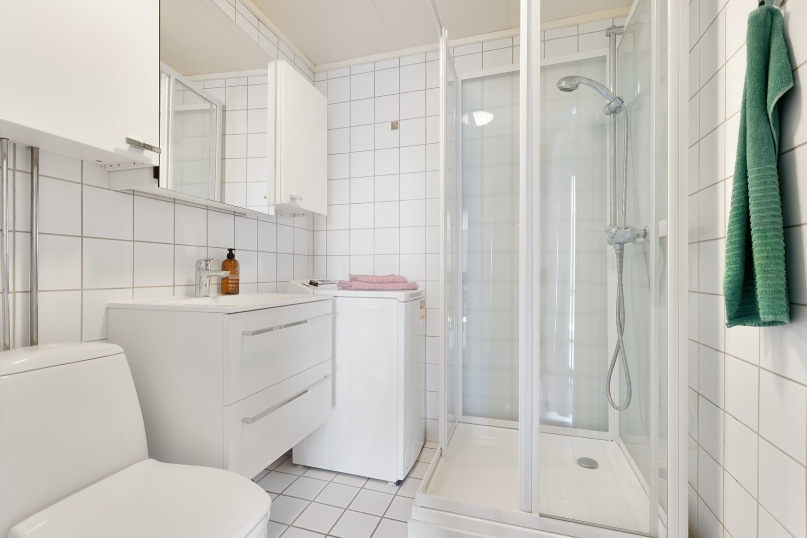 Badet er flislagt og har dusjkabinett, servant med ettgreps blandebatteri, og gulvstående toalett Galleribilde