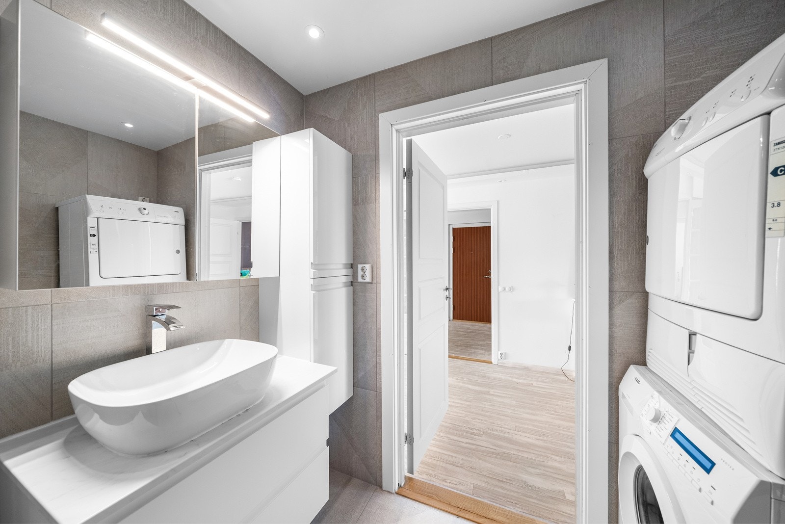 Badet er innredet med veggmontert klosett, nedsenket vask med speil og innredning, samt opplegg for både vaskemaskin og tørketrommel. Galleribilde