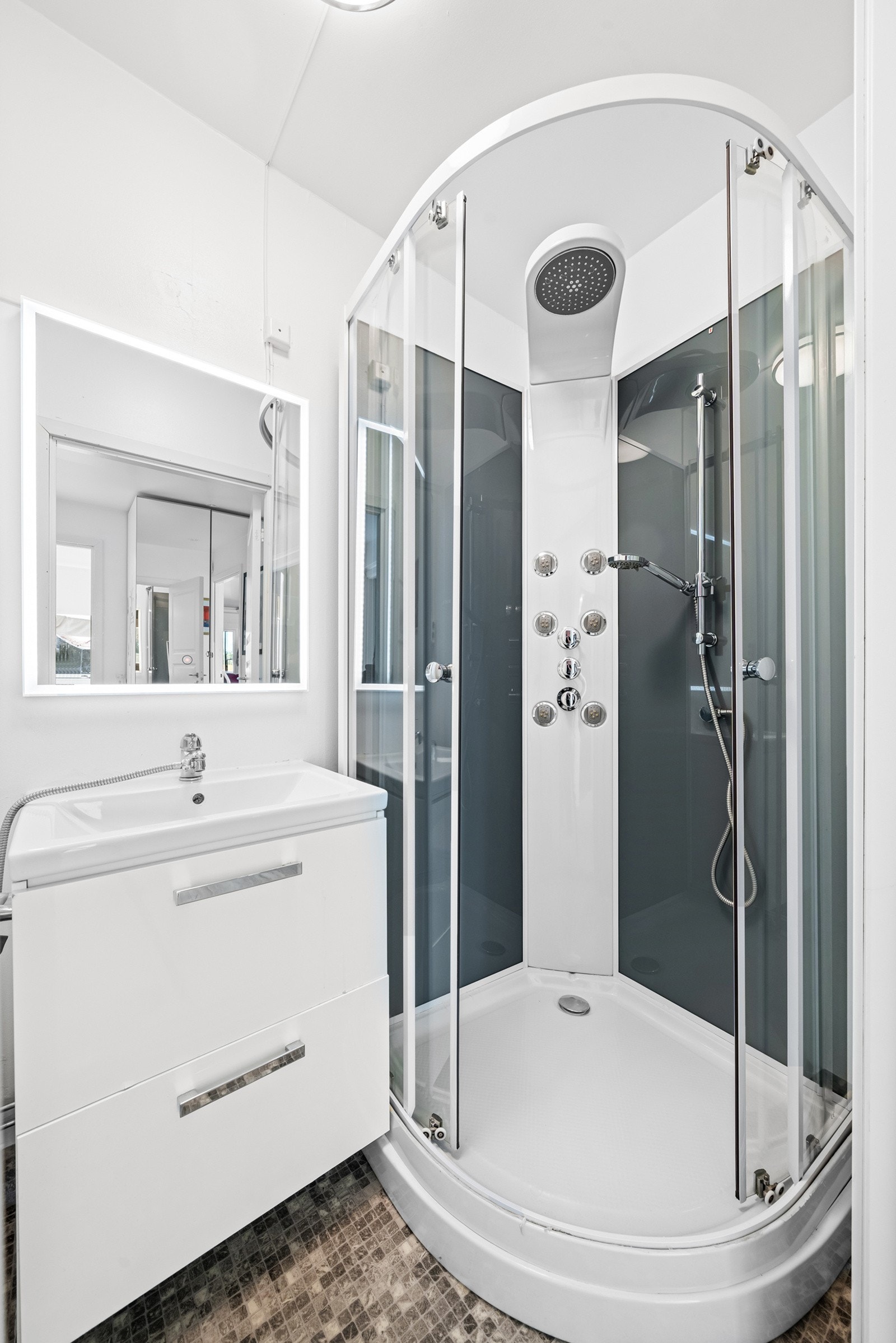 Rommet er utstyrt med dusjkabinett, håndvask med underskap og speil, samt et gulvmontert klosett. Galleribilde