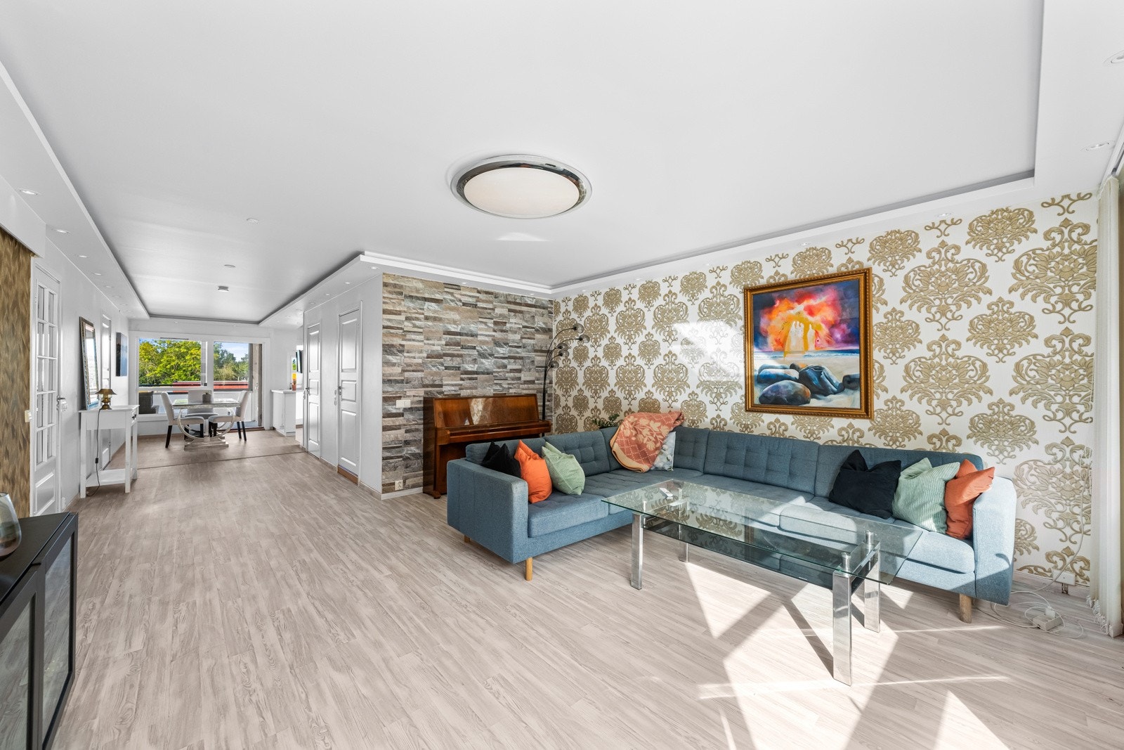 Med naturlige møbleringssoner har du god plass til både sofa og medievegg. En kontrastvegg med et mønstrete tapet tilfører et stilig element til rommet, mens de øvrige lysmalte veggene skaper et rent og rolig uttrykk. Galleribilde