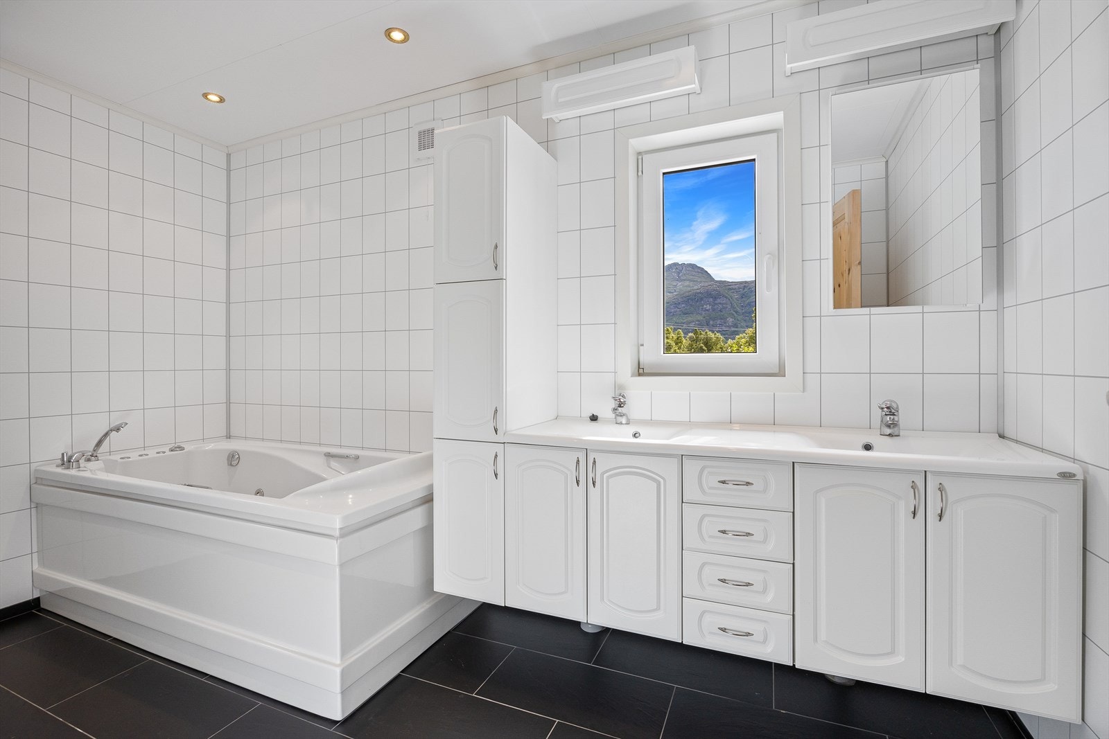 Bad 1 består av helfliset gulv og baderomsplater på vegg, toalett og badekar samt baderomsmøbel med dobbel vask. Galleribilde