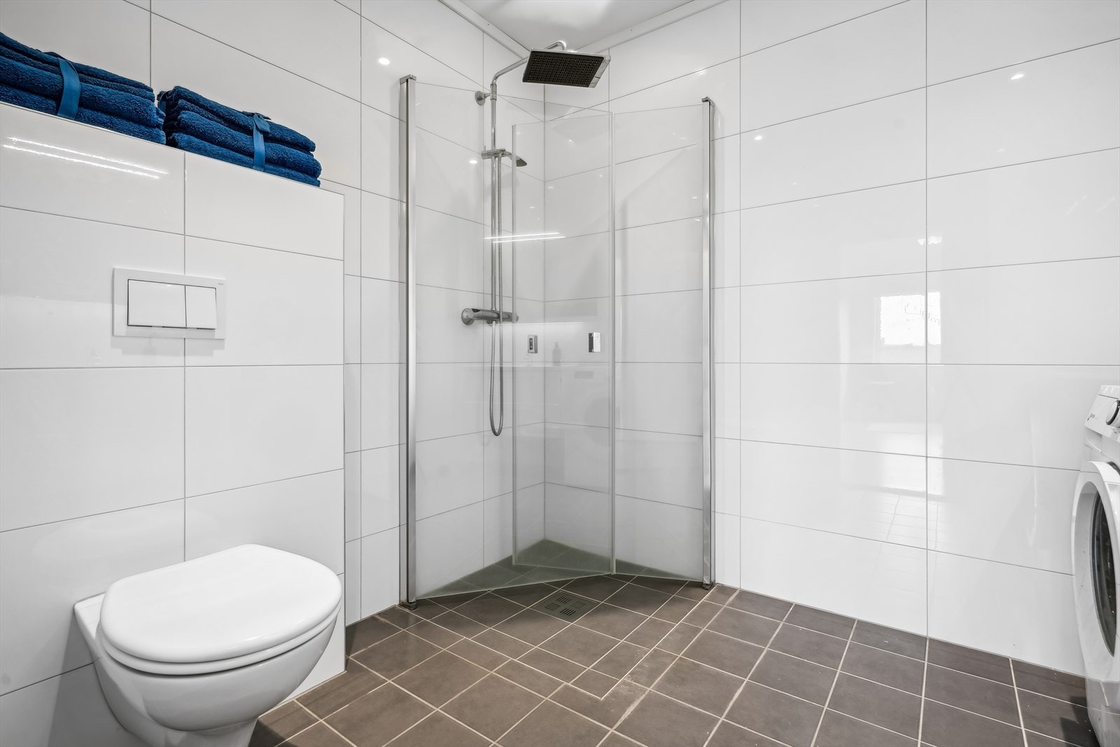 Dusj med innfellbare dører i herdet glass, servant i helstøpt plate, veggfestet klosett med innebygget sisterne og opplegg for vaskemaskin. Galleribilde