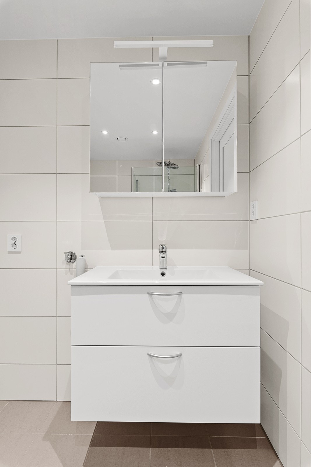 Et moderne og funksjonelt bad med dusjnisje, servant i innredning, vegghengt toalett og opplegg til vaskemaskin Galleribilde