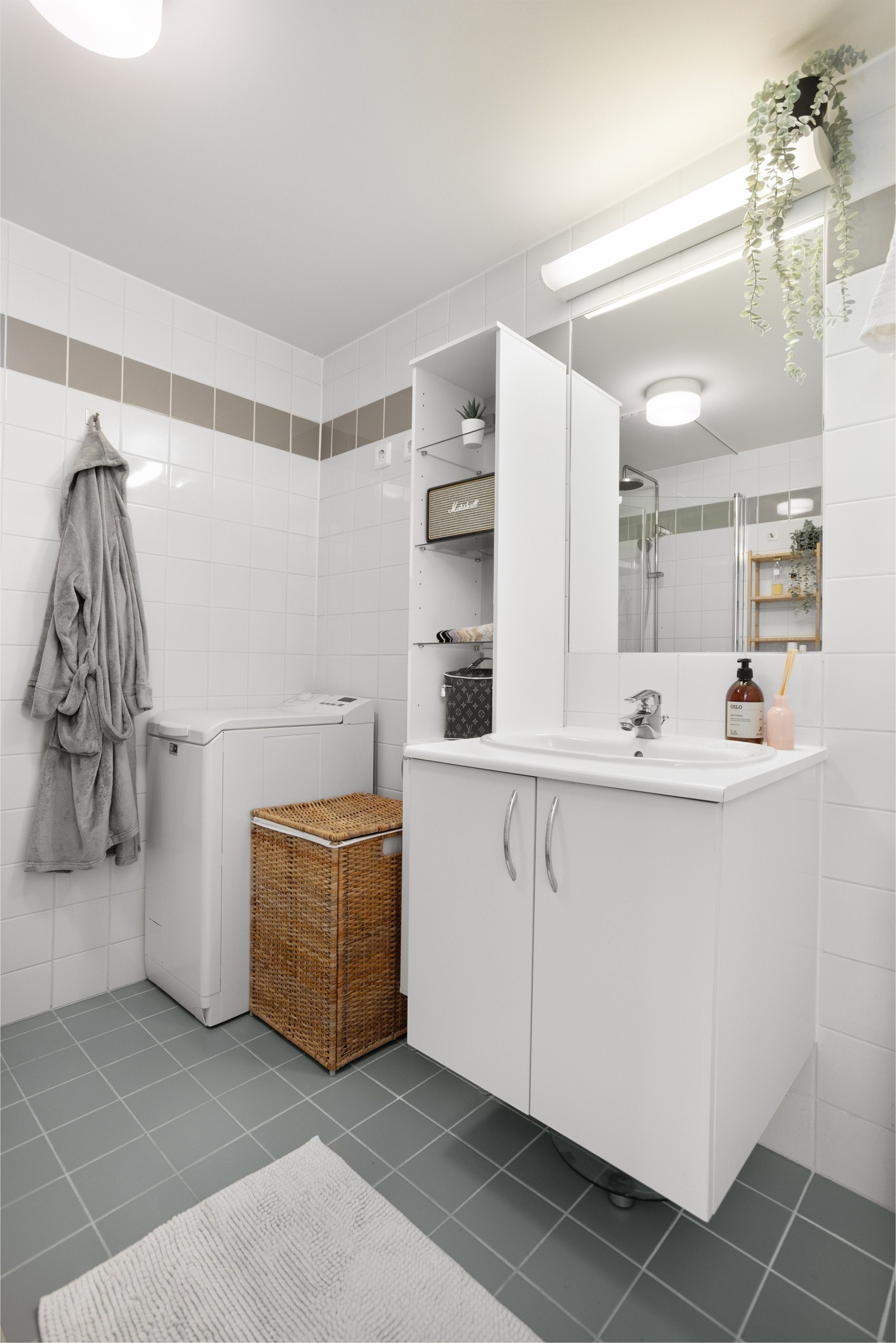 Tidløs baderomsinnredning med skuffer og heldekkende servant, speil med belysning over. Plass og opplegg for vaskemaskin. Galleribilde