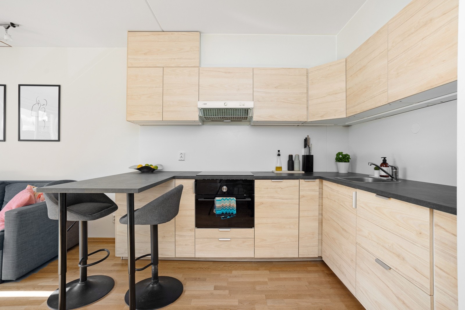 Moderne kjøkkeninnredning fra 2022 med glatte fronter i tremønstret utførelse og laminert benkeplate med nedfelt oppvaskkum. Praktisk med belysning under overskapene. Galleribilde