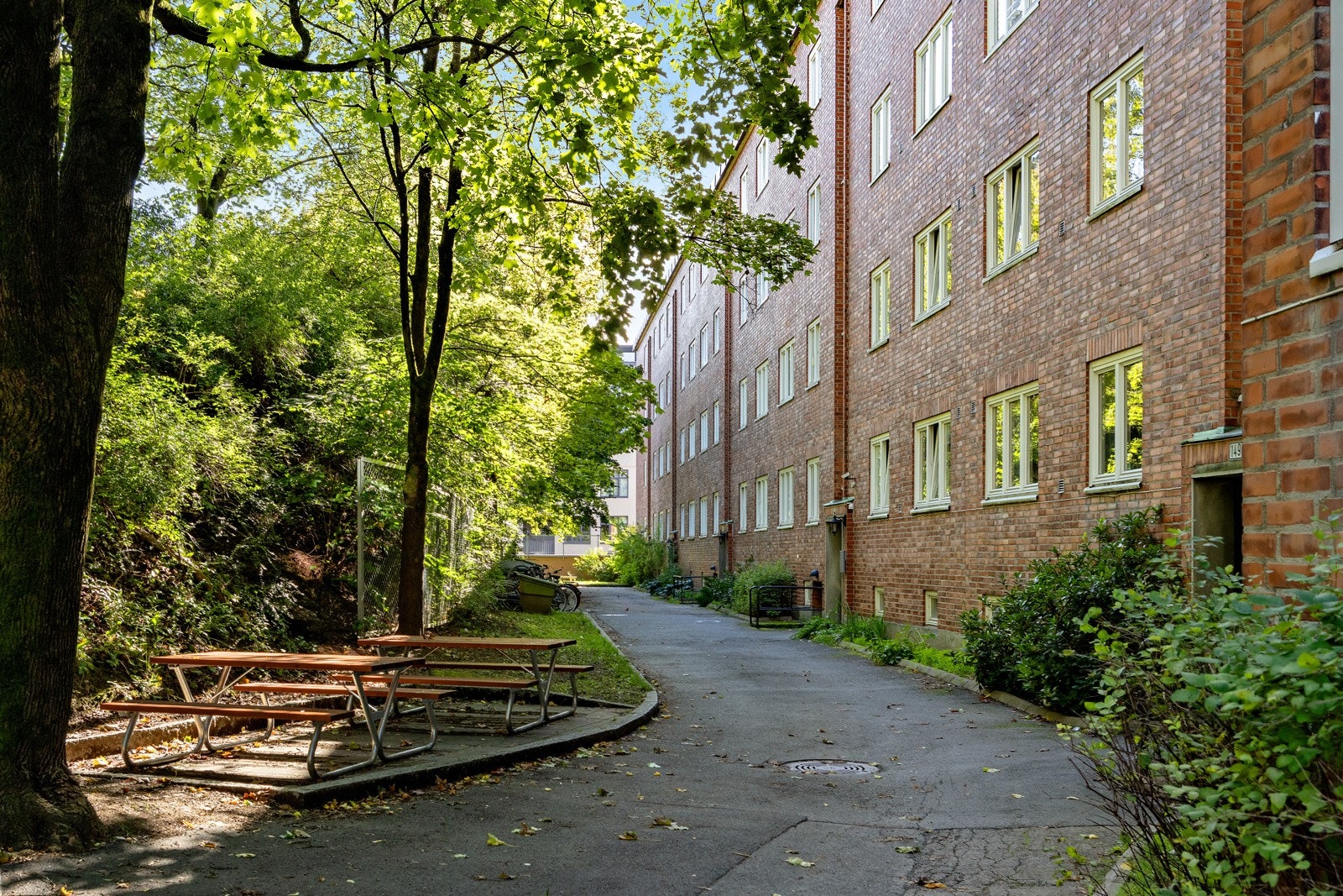 Fasade. Pent opparbeidet uteområde med sittebenker og asfaltert vei. Galleribilde