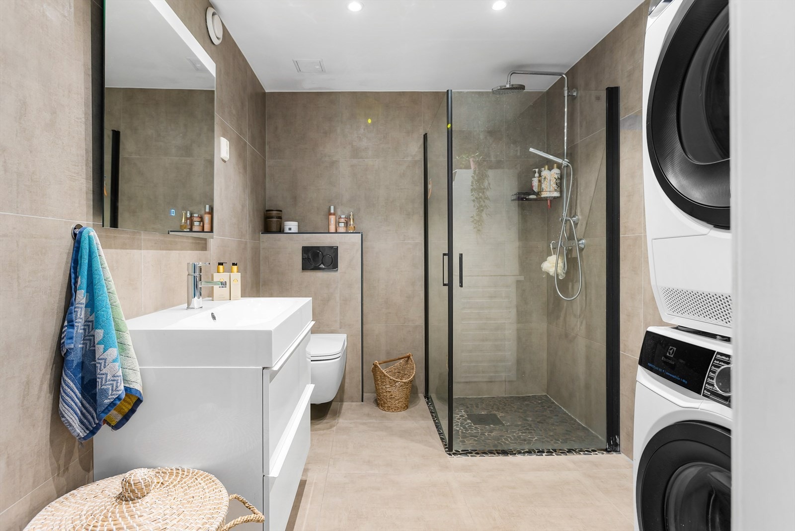 Badet har et moderne preg med store baderomsfliser. Det inneholder blant annet baderomsinnredning, toalett, dusj, samtidig som badet har opplegg for vaskemaskin og tørketrommel. Galleribilde