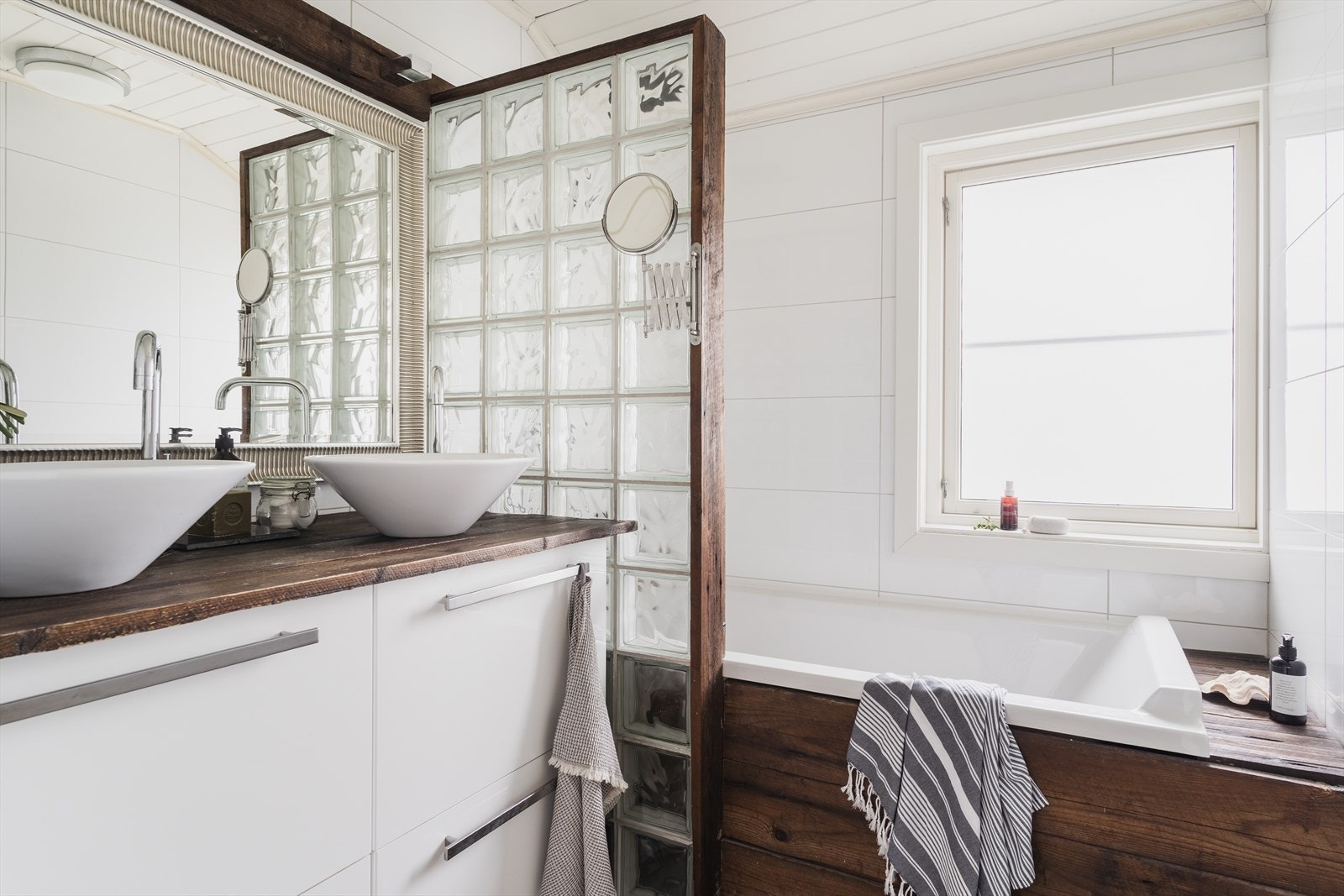 Badet er utstyrt med bred baderomsinnredning med to servanter, skuffer og vegghengt speil samt badekar Galleribilde