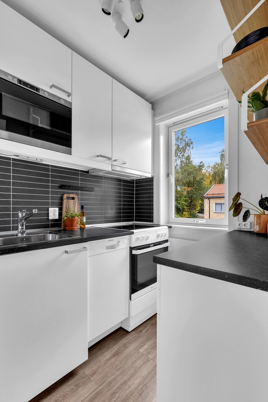 Kjøkkeninnredning med glatte fronter. Laminat benkeplate med nedfelt vaskekum. Våtromsplater og belysning over benkeplaten. Opplegg for vaskemaskin. Avtrekk over kokeplass. Galleribilde