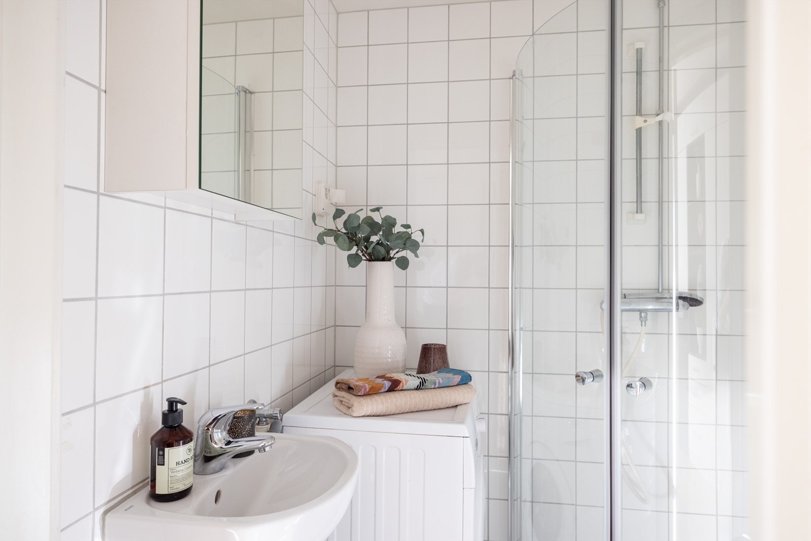 Badet er innredet med wc, servant nedfelt i innredning, speilskap og dusjhjørne med svingbare glassdører. Galleribilde