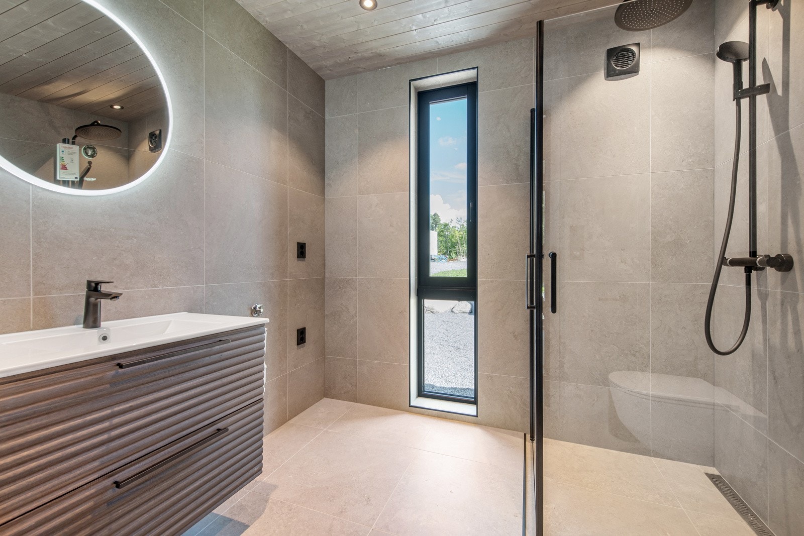 Delikat, flislagt bad med dusjhjørne, servant og toalett. Opplegg for vaskemaskin Galleribilde