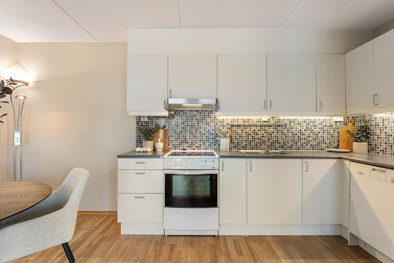 Lys og stilrent kjøkken bestående av glatte fronter og laminat benkeplate med nedfelt kum i rustfritt stål Galleribilde