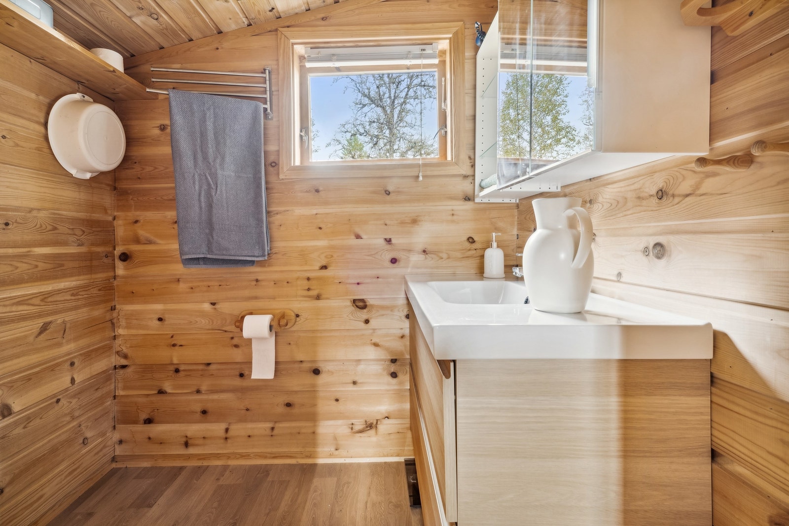 Stellerommet/vask har liggende panel på veggene og laminat på gulvet. Rommet er innredet med heldekkende servant i skuffeinnredning, speilskap og åpen hylleløsning. Galleribilde