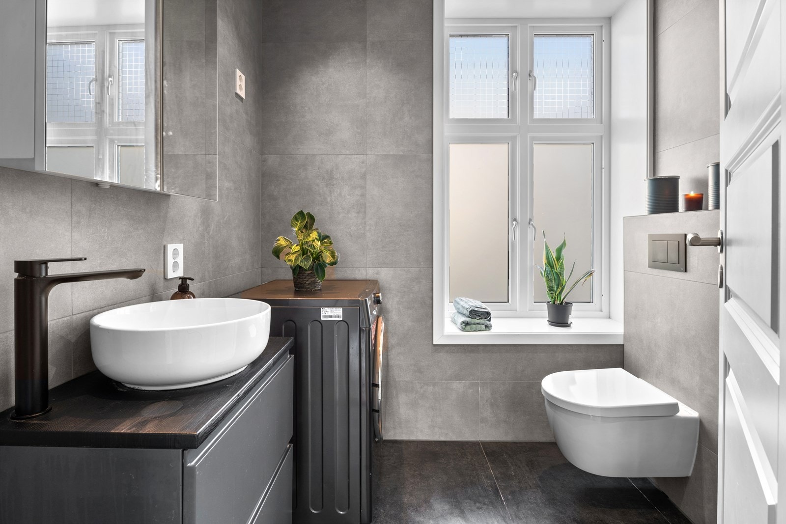 Nytt baderom fra 2023 bestående av et veggmontert toalett, en servantinnredning, et dusjhjørne med glassdører samt opplegg for vaskemaskin. Galleribilde