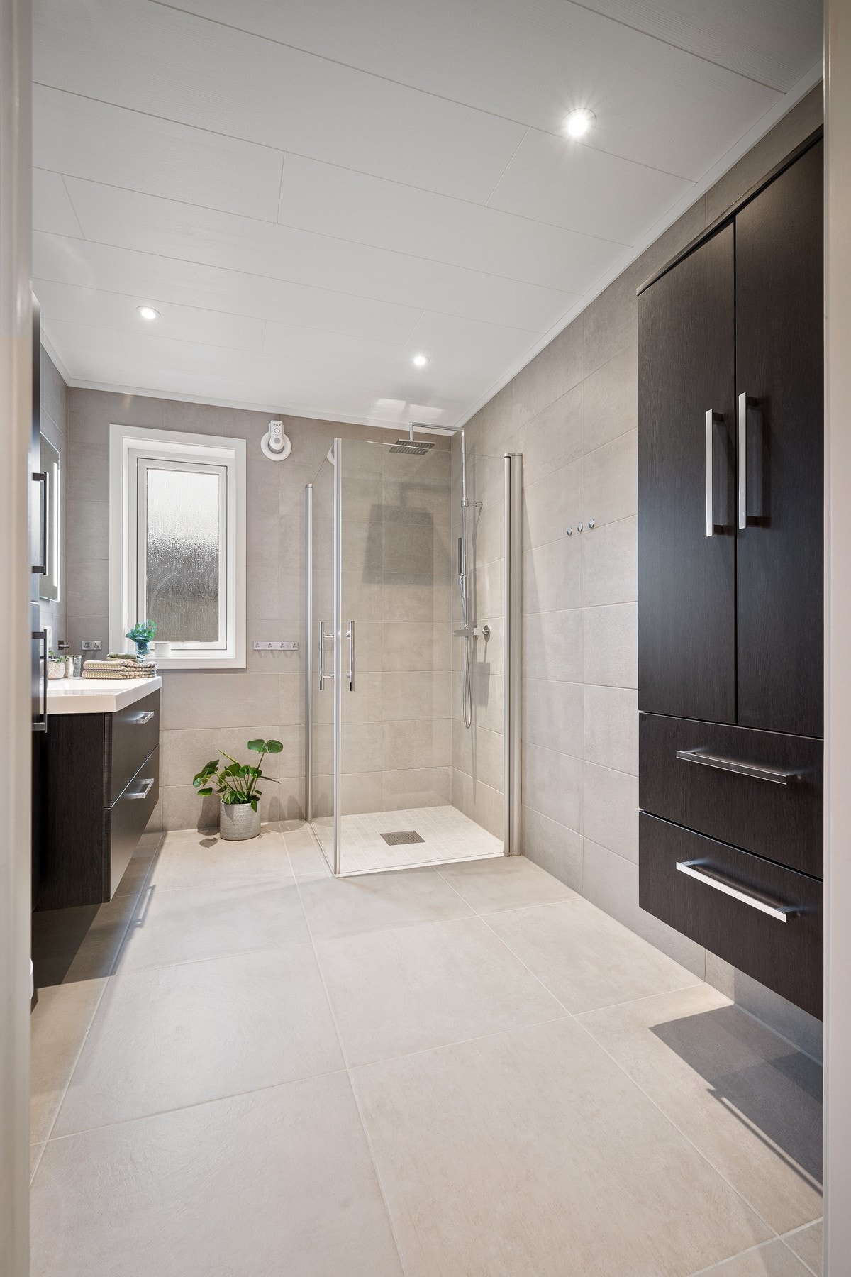 Dusjhjørne med glassvegger, vegghengt servantinnredning og høyskap, og vegghengt toalett Galleribilde