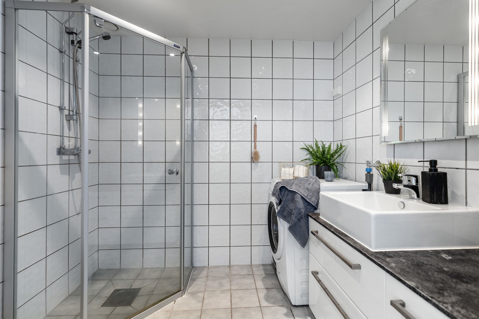 Innredningen består av et hvitt skuffemøblement med mørk benkeplate og toppmontert servant, og over servanten er det speil med integrert belysning. Galleribilde