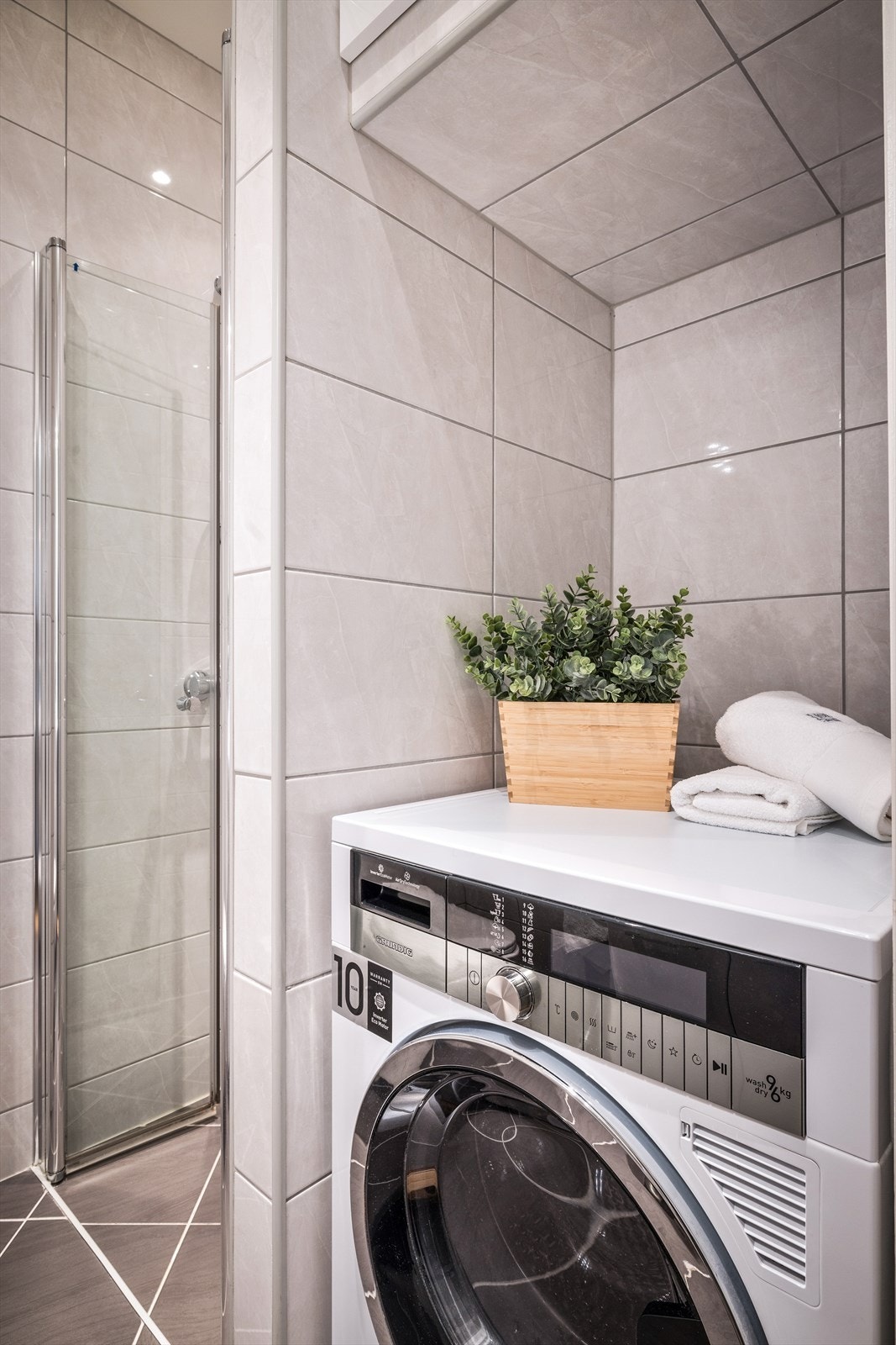 Badet er innredet med servant i møblement, speil med sideskap, vegghengt toalett, dusjhjørne og opplegg for vaskemaskin. Galleribilde