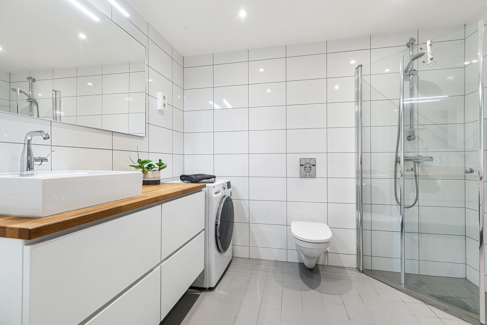 Badet har veggmontert toalett, dusjhjørne, og opplegg for vaskemaskin Galleribilde