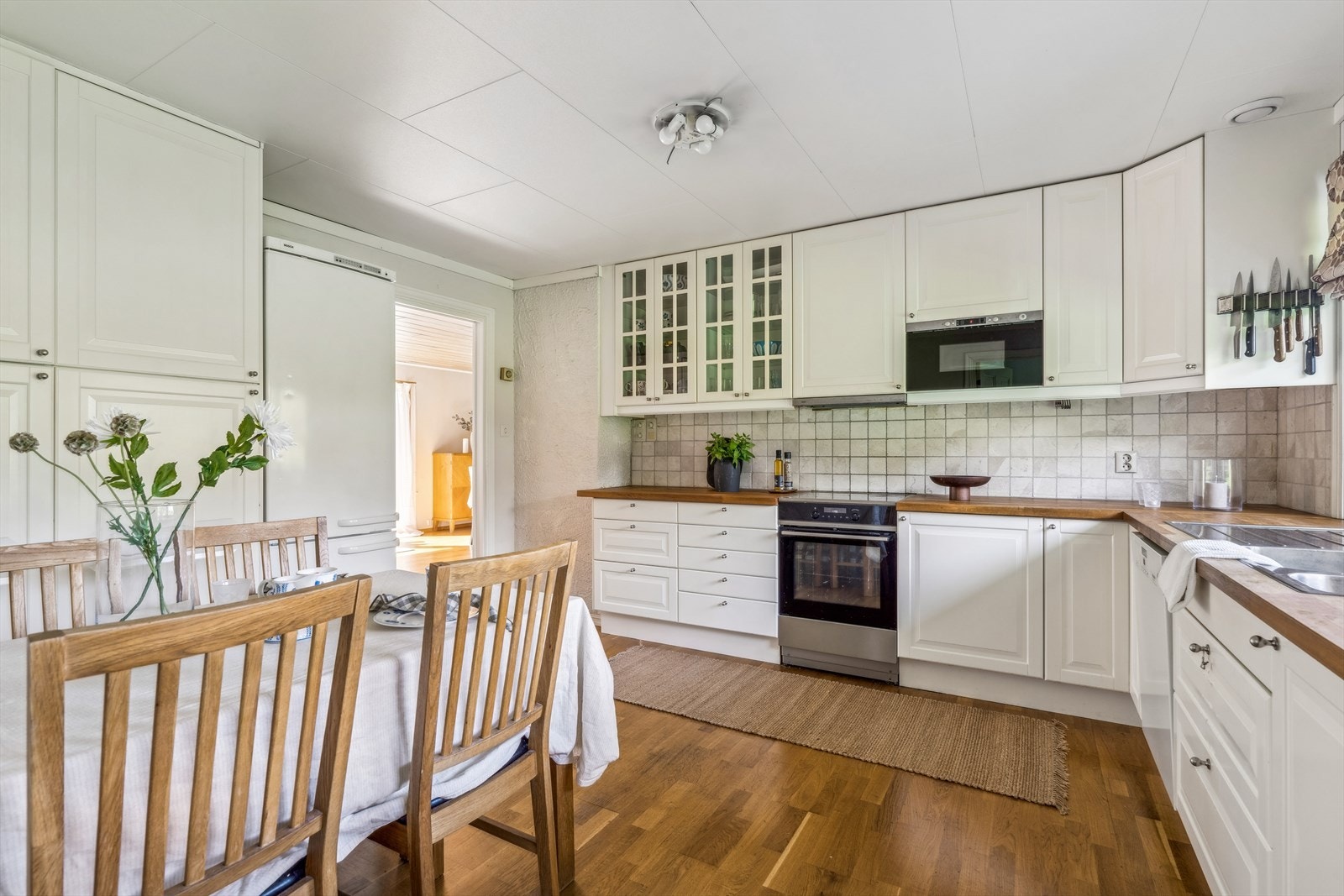 Delikat kjøkken med hvite profilerte fronter og benkeplate i heltre utførelse med oppvaskkum. Fliser montert som backsplash. Galleribilde