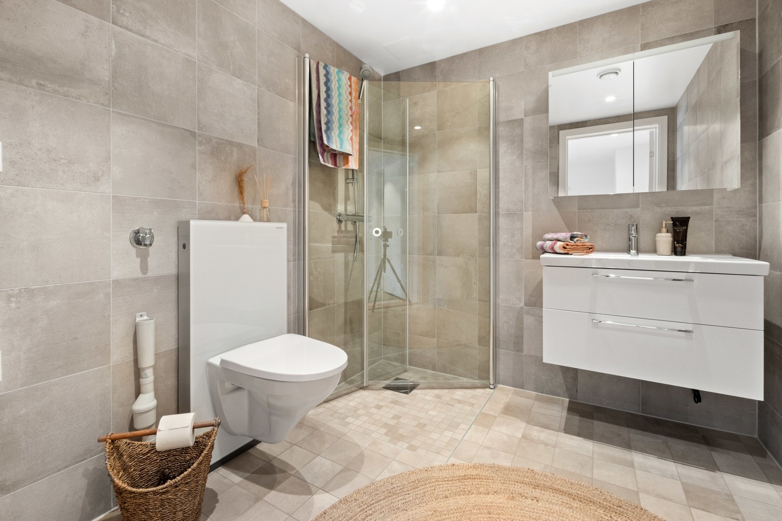 Delikat, flislagt baderom innredet med dusjnisje, servant med skuffeseksjon, klosett og opplegg for vaskemaskin. Galleribilde