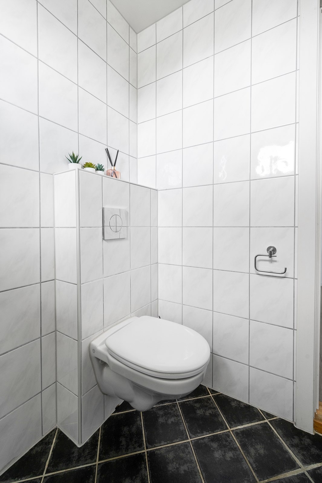 Videre består innredningen av dusjhjørne med glassdører og veggmontert dusjarmatur, vegghengt toalett. Avtrekksvifte plassert på vegg og opplegg for vaskemaskin. Galleribilde