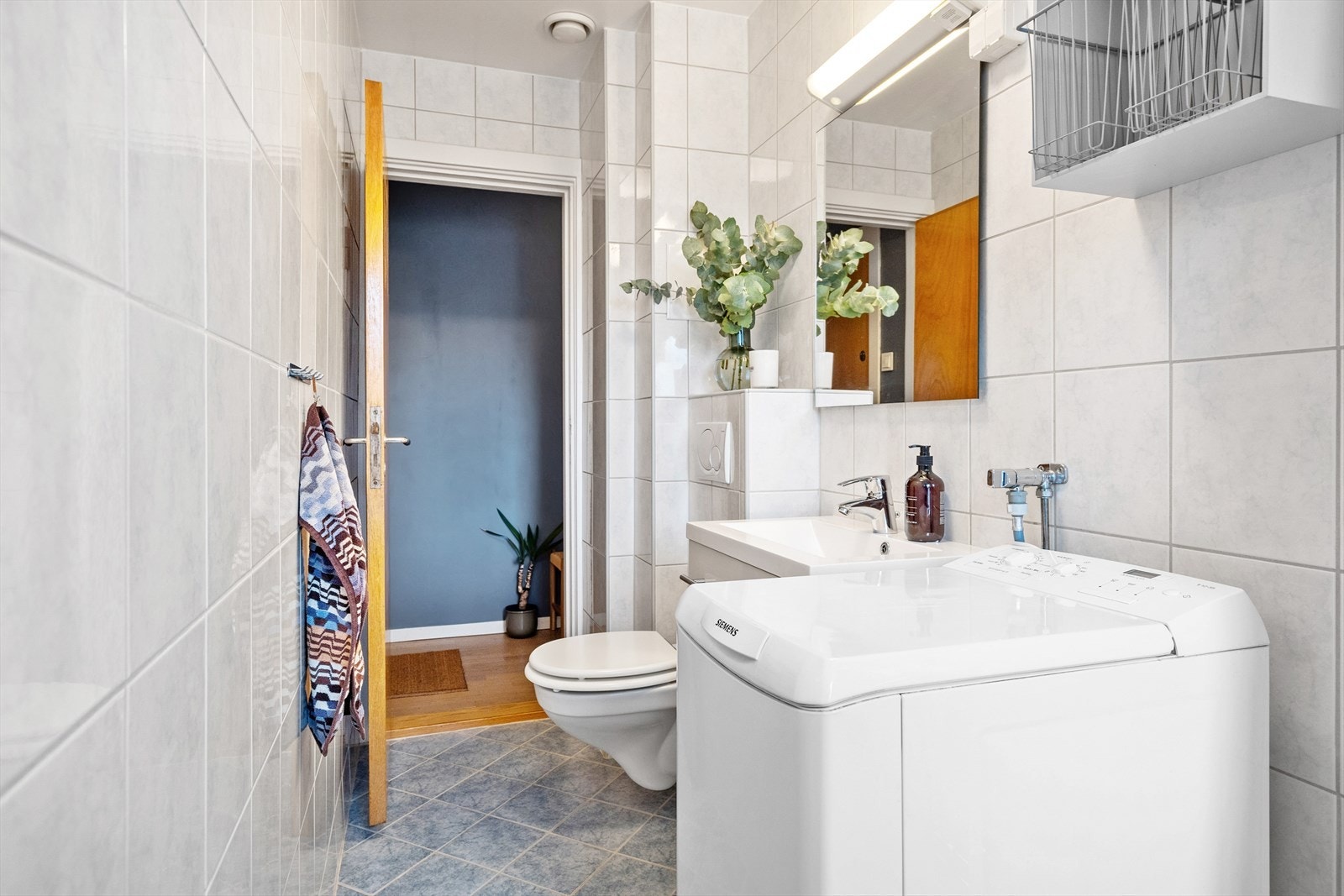 Badet inneholder veggmontert toalett, dusjhjørne med forheng og baderomsinnredning med skuffer, servant med ettgreps blandebatteri og speil Galleribilde