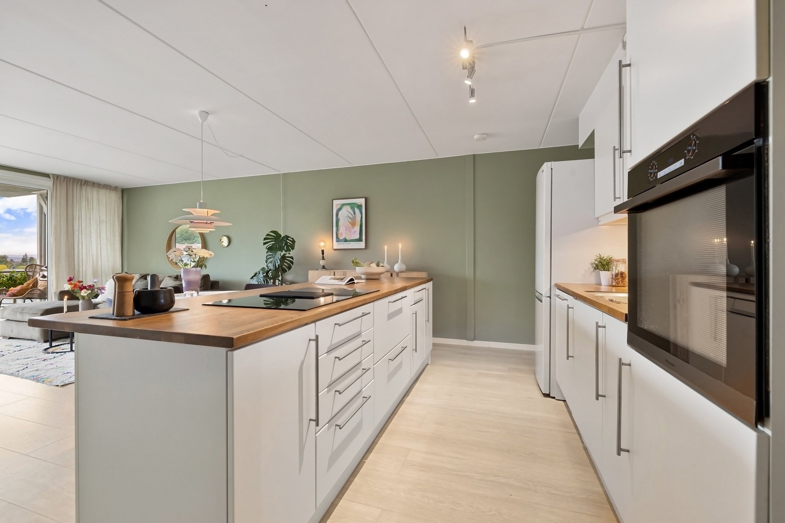 Kjøkkenet har hvite slette fronter, fliser mellom overskap og heltre benkeplate, nedfelt oppvaskkum med ett-greps blandebatteri samt belysning og stikkontakt under overskap. Galleribilde