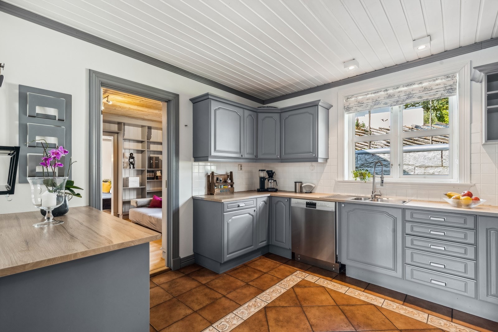 Kjøkkeninnredningen er pen med malte profilerte fronter i grå farge. Laminerte benkeplater med nedfelt oppvaskkum med avrenningsplate, samt lys under overskap. Malte fliser på vegg mellom overskap og kjøkkenbenk. Galleribilde