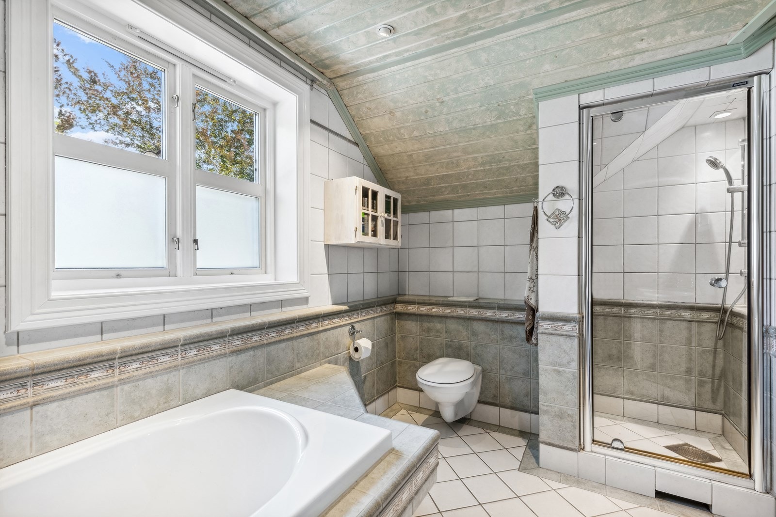 Badet er innredet med: skjermet dusjhjørnet, vegghengt toalett, flislagt servantinnredning med nedfelt 2 stk. servanter, innmurt speil på vegg over servant og Innfliset boblebadekar. Galleribilde