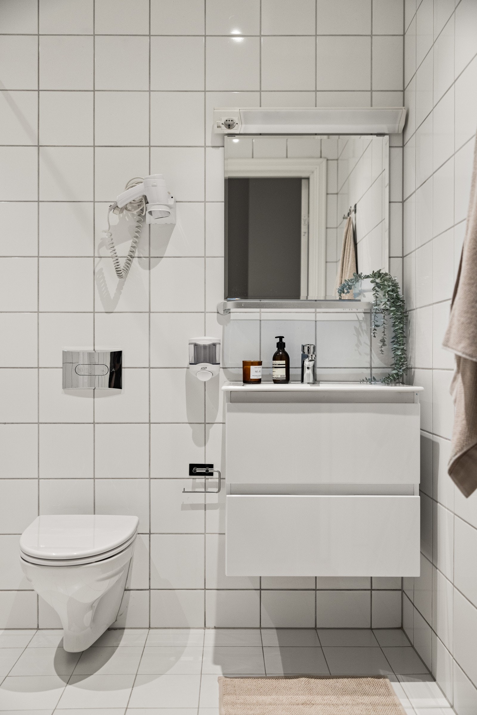 Moderne baderomsinnredning med skuffer og ovenpåliggende servant, glasshylle og speil med belysning over, samt vegghengt hårføner. Galleribilde