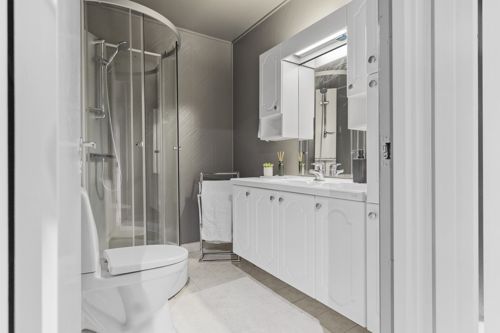 Badet har fliser på gulv med gulvvarme og tapet på vegger. Galleribilde