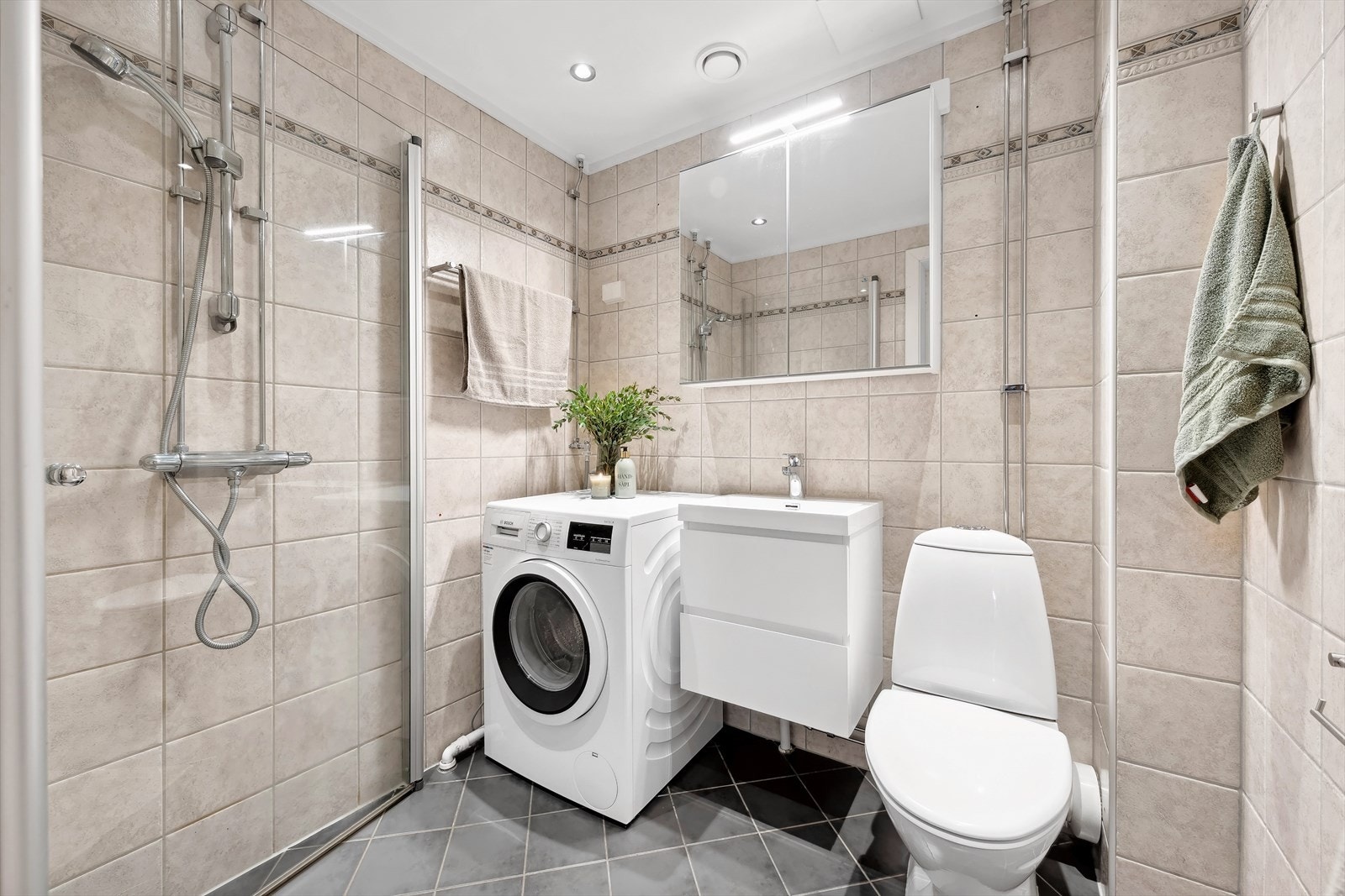 Pent flislagt baderom fra 2006 med innredning i glatte fronter, belysning over servant, dusj med innfellbare glassdører, gulvstående klosett og opplegg for vaskemaskin. Det er varme i gulv. Galleribilde