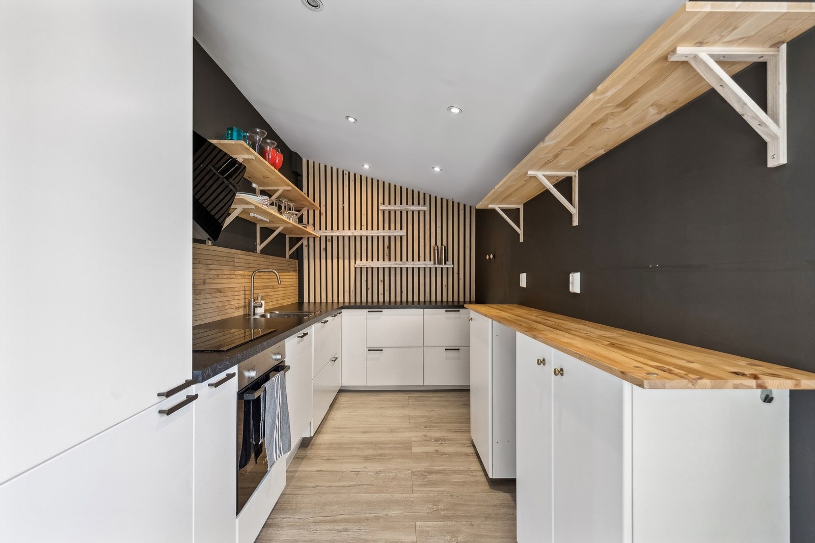 Nyere kjøkkeninnredning besådende av profilerte fronter, laminat benkeplate med planlimt kum i rustfritt stål og ventilator. Galleribilde