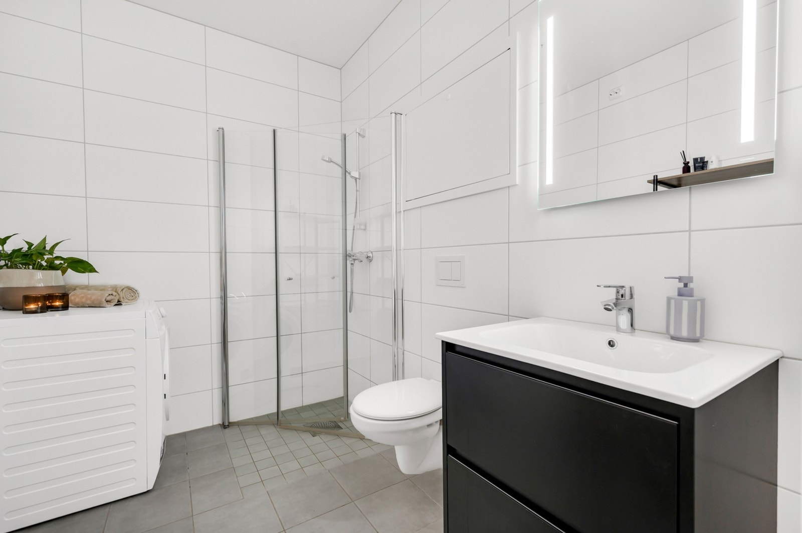 Lyst flislagt bad på ca. 5m² med romslig dusjnisje og opplegg for vaskemaskin. Galleribilde