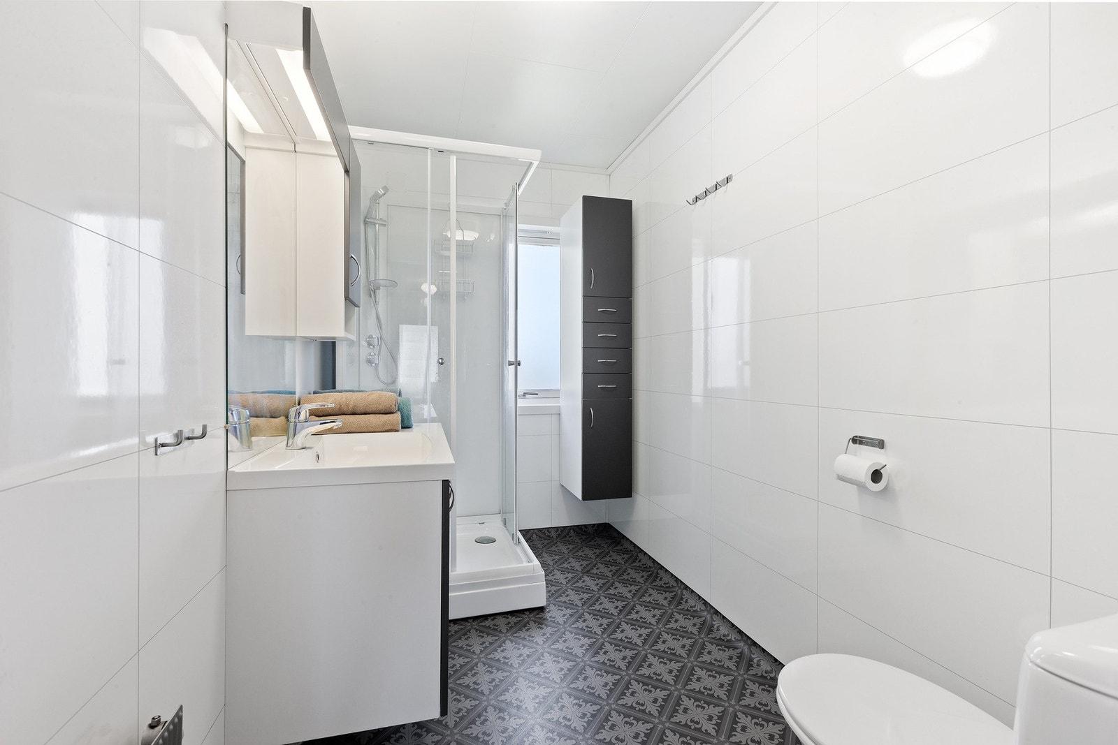 Badet har mørk innredning med nedfelt servant og skap under, overskap med speil og lys over. Dusjkabinett og toalett. Galleribilde