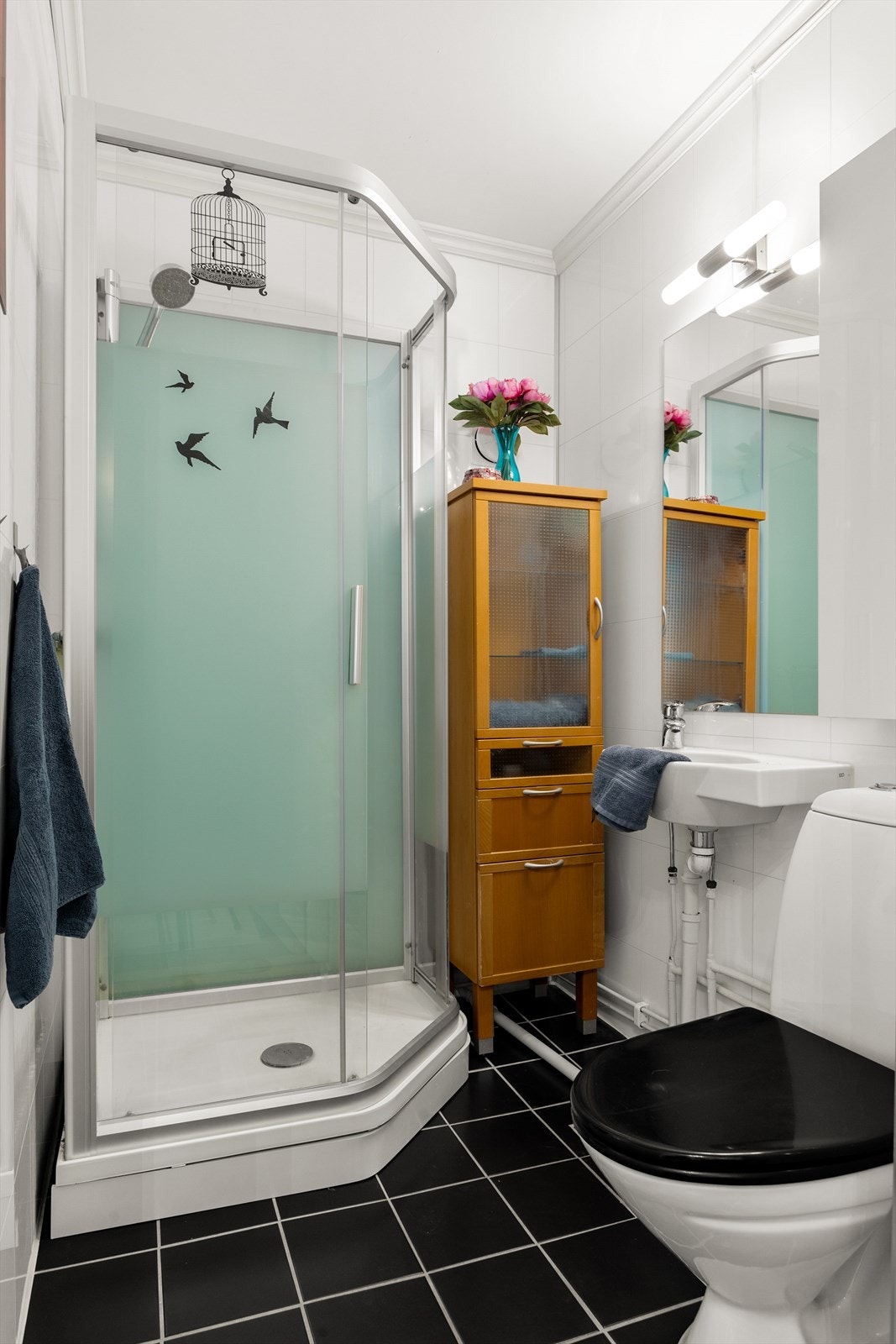 Boligen har to bad, ett i hver etasje. Badet i 1 etg. har svarte fliser på gulv og hvite baderomsplater på vegger. Det består av et gulvstående toalett, overskap, servant, speil, lys, stikk og ett dusjkabinett. Galleribilde