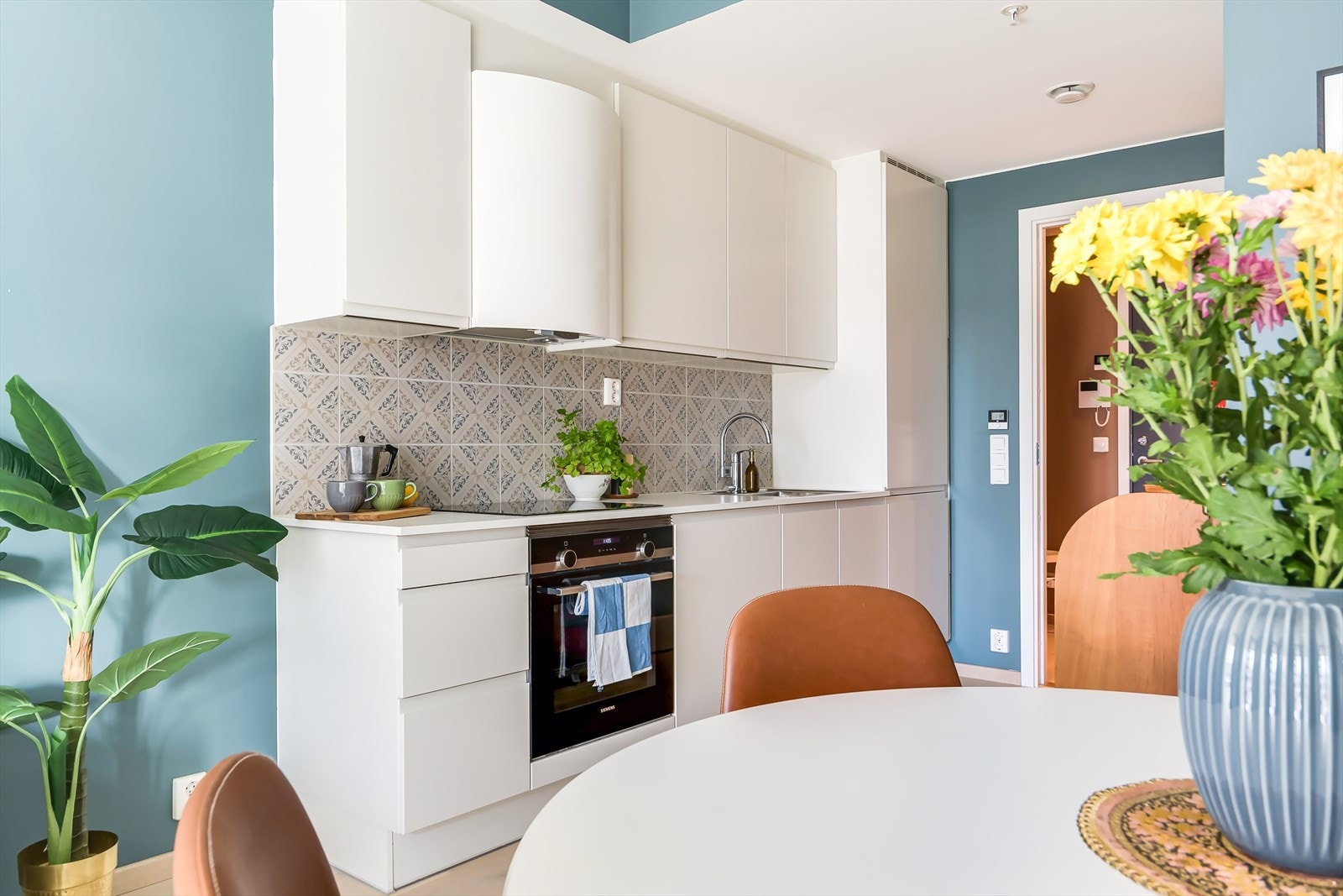 Lekkert HTH-kjøkken innredet med hvite, slette fronter og laminert benkeplate, samt stilfulle fliser mellom benkeplate og overskap Galleribilde