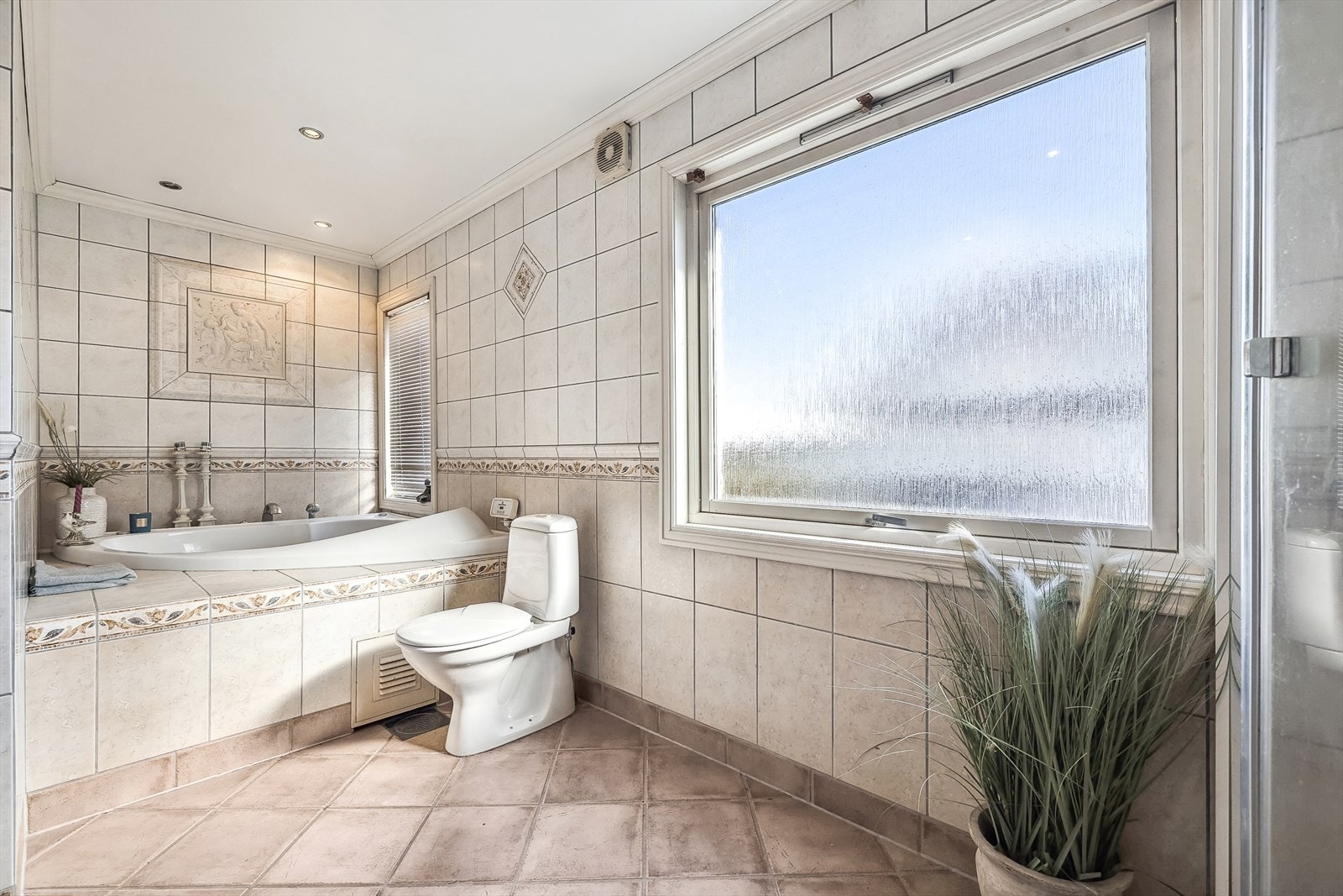 Badet har flislagte overflater, innebygget badekar, dusjkabinett, toalett og servantinnredning. Galleribilde