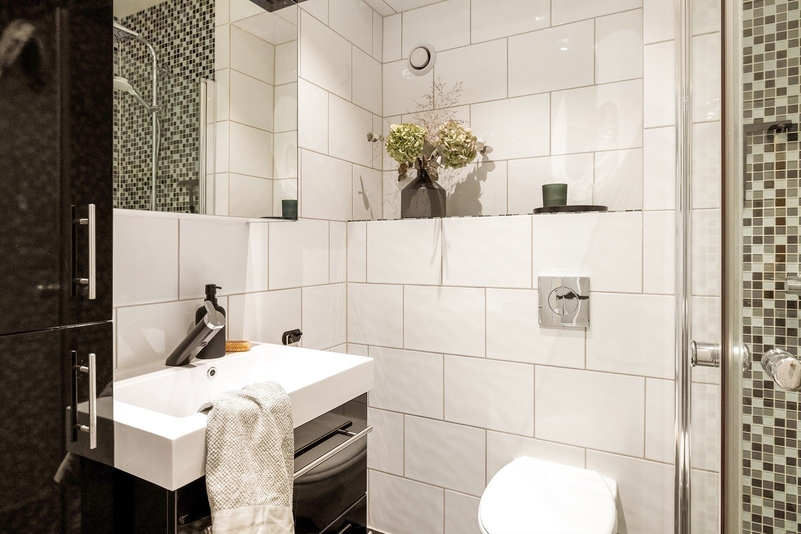 Badet er innredet med en dusjnisje med glassvegg, vegghengt toalett og en funksjonell baderomsinnredning som gir god plass til oppbevaring av nødvendige toalettsaker. Galleribilde