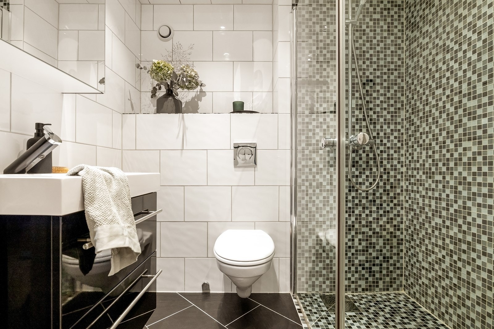 Badet er 2,8 kvm, og fremstår moderne med helflisede vegger og gulv, samt mosaikkfliser i dusjsonen som gir et pent uttrykk. Galleribilde