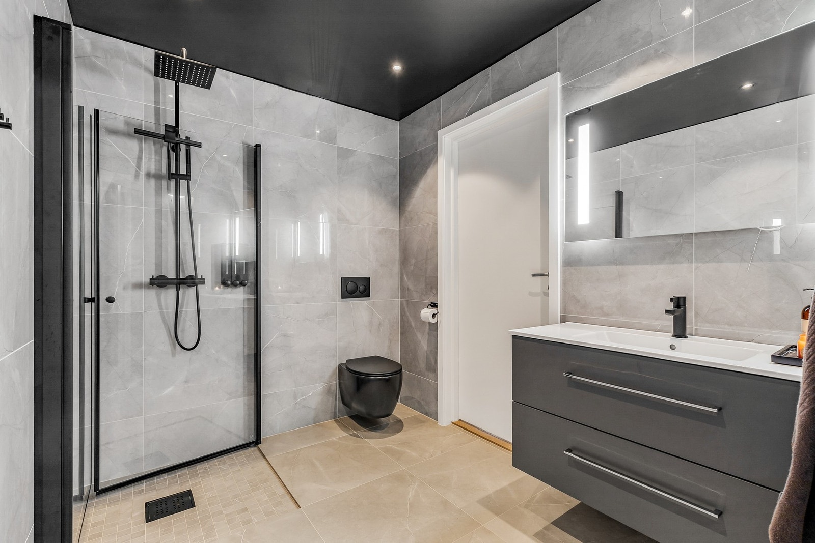 Pent bad med grå innredning med nedfelt servant, veggmontert toalett og dusjhjørne med svart armatur Galleribilde