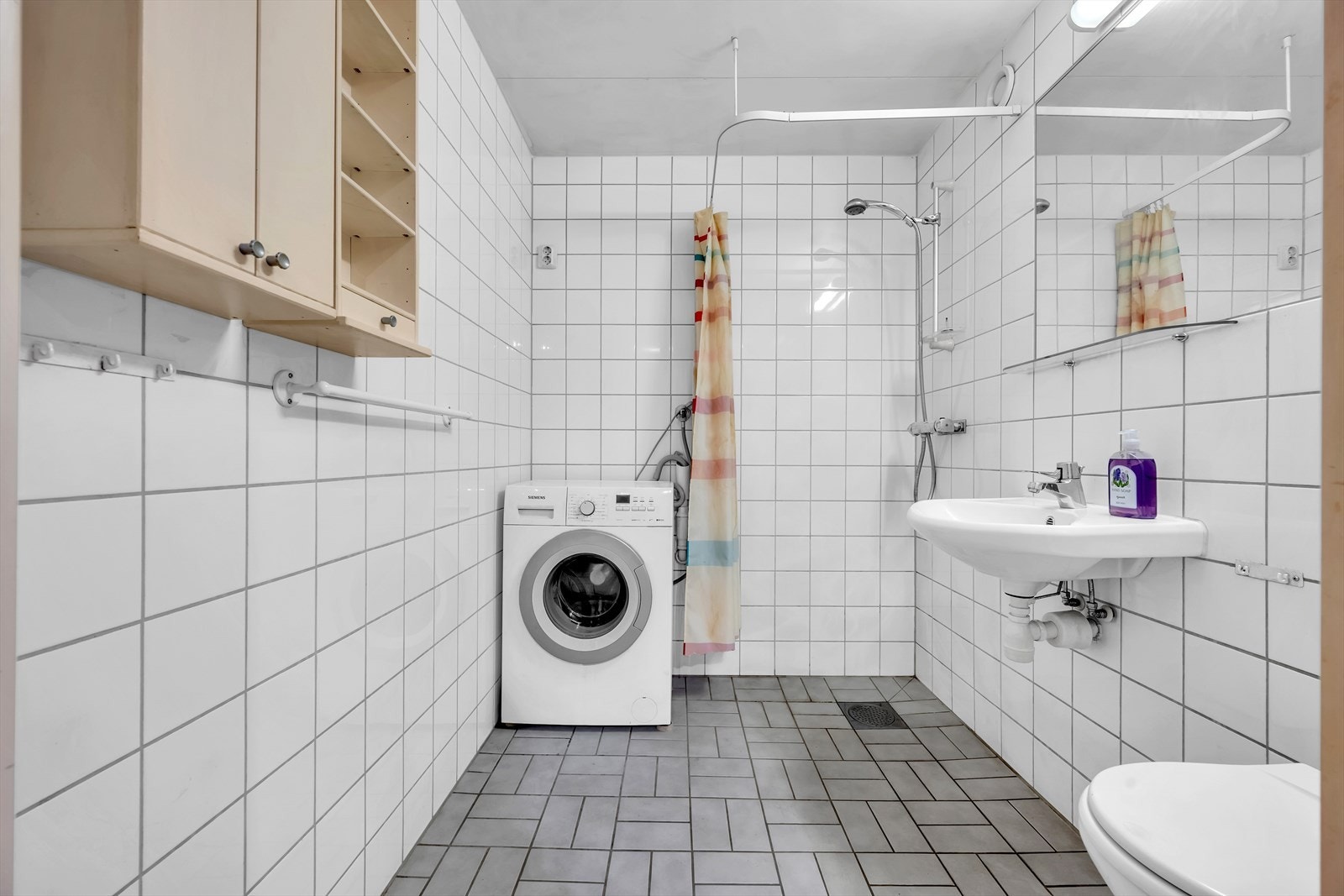 Lyst flislagt baderom med opplegg for vaskemaskin Galleribilde