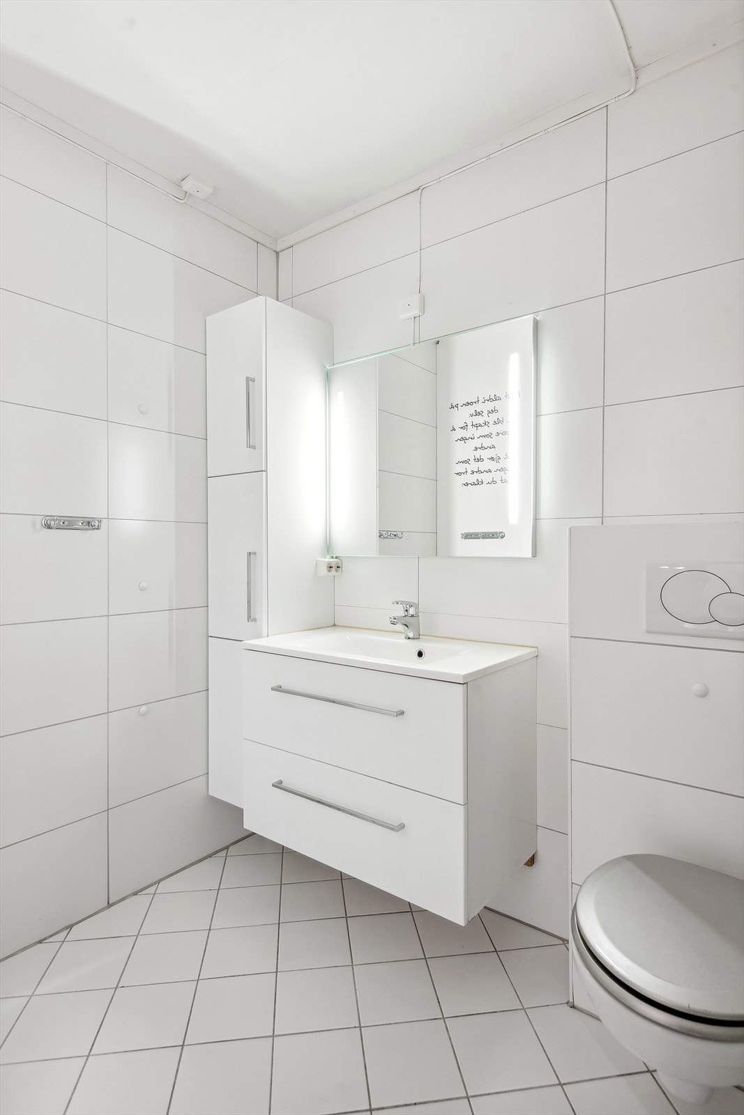 Badet har vegghengt servantinnredning med ovenpåliggende servant og speil med belysning, vegghengt høyskap, vegghengt toalett og dusjnisje med vegger. Galleribilde