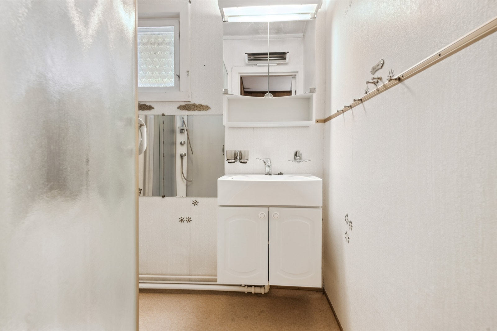 Eldre bad med dusjkabinett, servant med underskap og speilskap. Oppvarming med stråleovn på vegg. Badet bør renoveres. Galleribilde