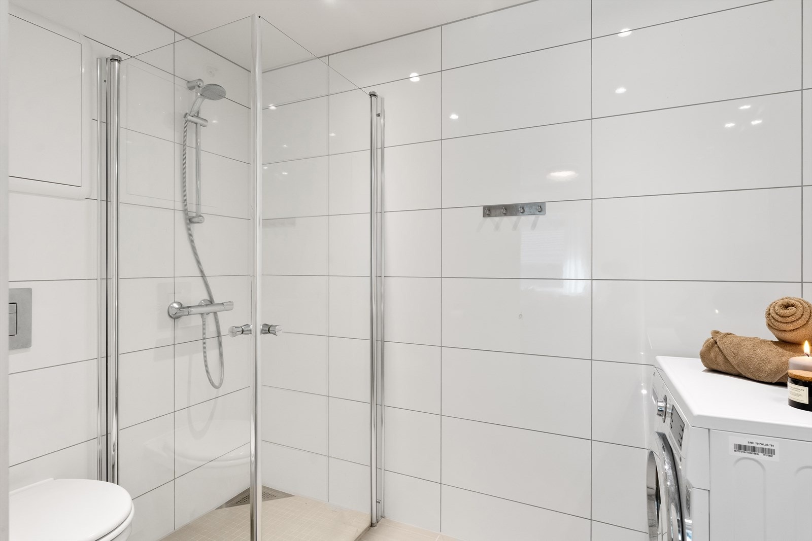 Badet er utsyrt med heldekkende servant, servantskap, speilskap, veggmontert toalett og to svingbare dusjvegger. Det er opplegg for vaskemaskin. Galleribilde