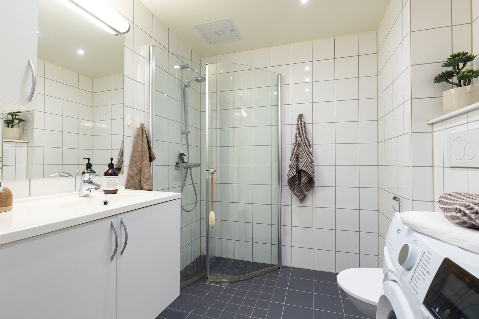 Delikat, flislagt baderom med gulvvarme og downlightsbelysning. Baderommet har en romslig skapinnredning med lyse fronter med servant, samt speil og belysning over. Galleribilde