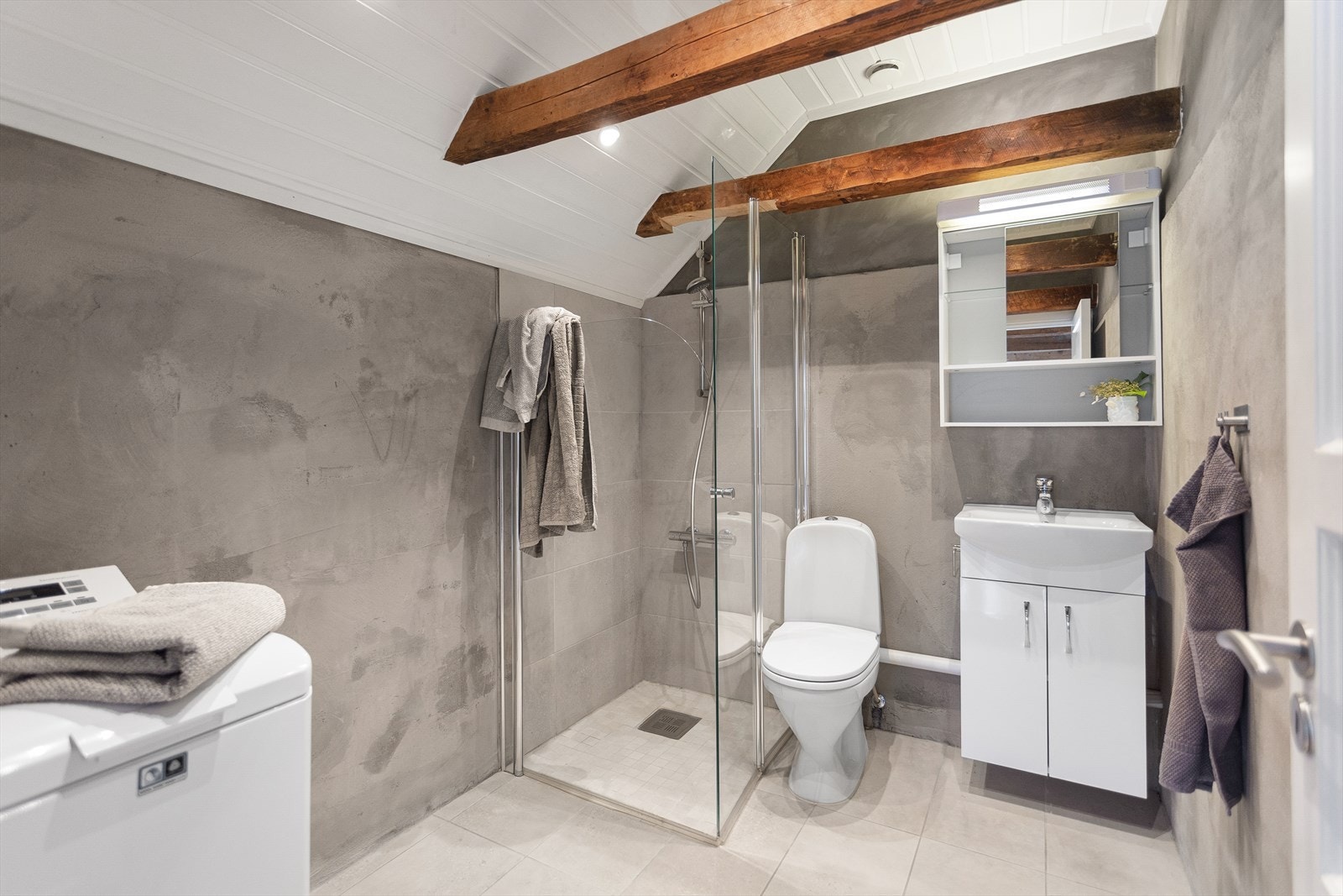 Badet i loftsetasjen er fra 1996 med wc, servantskap, dusj i hjørne med innadslående dører og opplegg for vaskemaskin. Videre er det veggflater med microsement og fliser i dusjsonen. Galleribilde